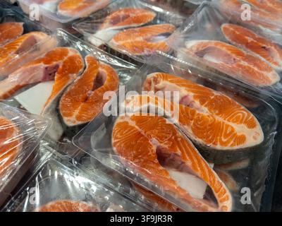 Portionierte rohe Lachsfilets, verpackt in transparenten versiegelten Schalen auf einem Einzelhandelsregal, die gesunde Bio-Lebensmitteloptionen für nahrhafte Hausmannskost darstellen Stockfoto
