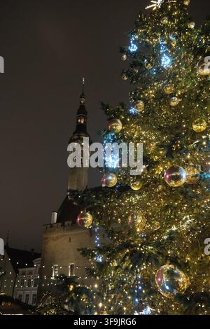 Niedriger Winkel eines beleuchteten Weihnachtsbaums mit dem Turm des Tallinner Rathauses im Hintergrund bei Nacht Stockfoto