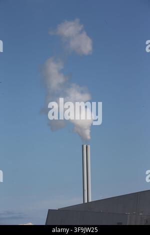 Dublin, Leinster, Irland, 15. Aug. 2026 – Die eckige Dublin Waste to Energy-Anlage steht auf der Poolbeg-Halbinsel neben der Dubliner Bucht, mit einer weißen Dampfwolke, die aus ihren Schornsteinen aufsteigt, und den roten und weißen Poolbeg-Schornsteinen im Hintergrund. Die Anlage behandelt Restmüll und gewinnt Energie zurück und ist seit 2017 in Poolbeg in Betrieb; im Dezember 2025 erreichte sie eine kumulierte Menge von fünf Millionen Tonnen an Restmüll. Stockfoto