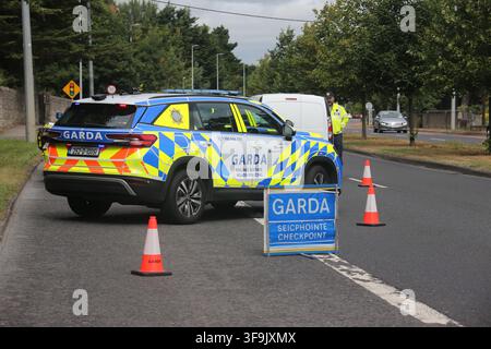 Clondalkin, Dublin, Irland, 15. Aug. 2026 – Ein markiertes Garda Roads Policing SUV, ein uniformierter Garda-Beamter in Warnkleidung, Verkehrskegel und ein zweisprachiges Garda Seicphointe Checkpoint-Schild sind auf der R113 positioniert. Die Gardaí richteten eine Straßenkontrolle auf der Strecke durch Clondalkin ein; der spezifische Zweck der Operation und etwaige Durchsetzungsmaßnahmen wurden nicht mitgeteilt. Das Bild dokumentiert die Verkehrskontrolle, Verkehrsmanagement und öffentliche Sicherheitsüberwachung im Vorort von Dublin. Die R113 führt durch Clondalkin. Stockfoto