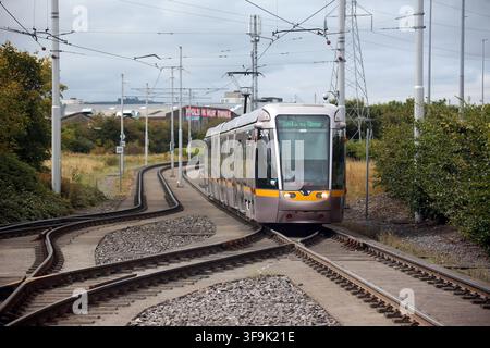 Tallaght, County Dublin, Irland, 15. Aug. 2026 – Das markante weiße Spannzelt, die Inselplattformen, die Oberleitungen, die Richtungsschilder und die Fahrkartenvalidierer am Belgard Luas-Halt der Roten Linie in Dublin. Belgard dient als Kreuzungspunkt für Straßenbahnlinien in Richtung Tallaght und Saggart, mit Fahrten in Richtung Stadtzentrum von Dublin in die entgegengesetzte Richtung. Der Halt wurde für den Saggart-Zweig mit einem zusätzlichen Gleis, veränderten Plattformen und einem das Inselplattformen überspannenden Dach neu konfiguriert, was seine Rolle als Stadtbahn-Interchange im Südwesten Dublins stärkte. Stockfoto
