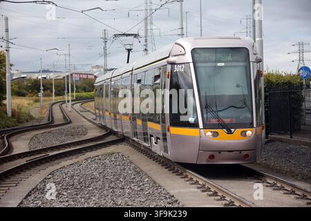 Tallaght, County Dublin, Irland, 15. Aug. 2026 – Das markante weiße Spannzelt, die Inselplattformen, die Oberleitungen, die Richtungsschilder und die Fahrkartenvalidierer am Belgard Luas-Halt der Roten Linie in Dublin. Belgard dient als Kreuzungspunkt für Straßenbahnlinien in Richtung Tallaght und Saggart, mit Fahrten in Richtung Stadtzentrum von Dublin in die entgegengesetzte Richtung. Der Halt wurde für den Saggart-Zweig mit einem zusätzlichen Gleis, veränderten Plattformen und einem das Inselplattformen überspannenden Dach neu konfiguriert, was seine Rolle als Stadtbahn-Interchange im Südwesten Dublins stärkte. Stockfoto