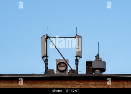 Dachfunktechnik mit Mobilfunkantennen, Kommunikationspanelen, Kabeln und Lüftungsstrukturen, die auf einem Backsteingebäude installiert sind Stockfoto