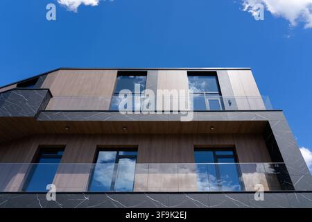 Moderne mehrstöckige Hausfassade mit Glasgeländern an den Balkonen vor blauem Himmel, Außenansicht einer Luxusresidenz, Foto aus einem nach oben gerichteten Winkel Stockfoto