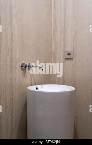 Zylindrisches weißes Waschbecken mit wandmontiertem Wasserhahn auf natürlichem Steinhintergrund, luxuriöses Badezimmer-Innenraum-Detailfoto Stockfoto
