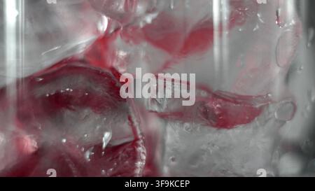 Rote Flüssigkeit, die über Eiswürfel in einem Glas fließt und einen erfrischenden kalten Getränke-Hintergrund erzeugt Stockfoto