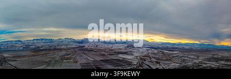 Panoramische Luftaufnahme zeigt schneebedeckte Berge und landwirtschaftliche Felder in Kirgisistan. Die ruhige Landschaft zeigt geometrische Muster der Felder Stockfoto