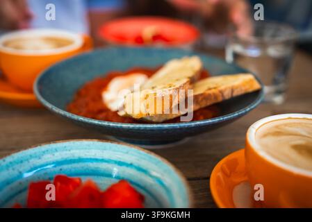Frühstückstisch mit Shakshuka, getoastetem Brot und Kaffee Stockfoto