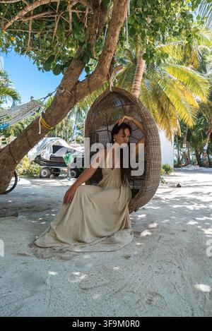 Frau sitzt in einem hängenden Korbstuhl auf der Insel Dhigurah Stockfoto