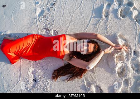 Frau in einem hellen Kleid, die auf dem weißen Sand eines Strandes auf den Malediven liegt Stockfoto