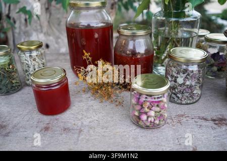 Eine Auswahl an klaren Gläsern, gefüllt mit verschiedenen getrockneten Kräutern, Blumen Tees und roten Kräuterölen, die auf einer Holzoberfläche ausgelegt sind. Stockfoto