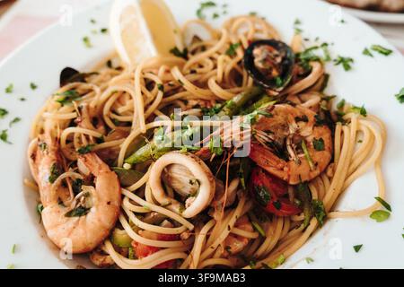 Meeresfrüchtespaghetti mit Garnelen, Muscheln, Tintenfischen, Gemüse und Zitrone wird auf einem weißen Teller serviert. Das Gericht eignet sich für Restaurant, Menü, Gourmet und Essens Stockfoto