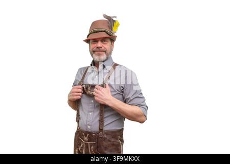 Ein lächelnder reifer Mann trägt einen bayerischen Hut und Lederhosen-Suspender auf einem schlichten Hintergrund. Stockfoto