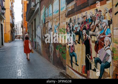 Mural von Musikern mit einer Frau, die die Gasse hinuntergeht. Carrer del Pintor Fillol, Barrio el Carmen, Valencia. Spanien. Stockfoto