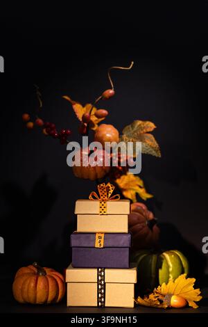 Vertikaler Stapel von Geschenkkisten mit Kürbissen, Beeren und Herbstblättern auf schwarzem Hintergrund für Halloween-Thanksgiving-Promotion Stockfoto