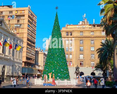 SANTIAGO, CHILE - 03. DEZEMBER 2025: Ein hoher geschmückter Weihnachtsbaum steht auf dem Plaza de Armas-Platz, umgeben von historischen Gebäuden und Palmen in San Stockfoto