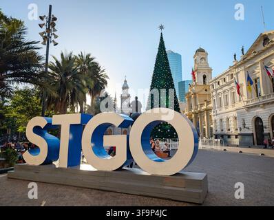 SANTIAGO, CHILE - 03. DEZEMBER 2025: Ein großes STGO-Schild steht in der Nähe eines hohen Weihnachtsbaums auf der Plaza de Armas mit historischen Gebäuden in der Nähe in Santiago, Chil Stockfoto