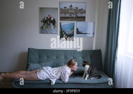 Zufriedene Tierbesitzerin spielt mit ihrer Katze auf der Couch zu Hause, Freundschaft und Bindung zwischen Mensch und Tier als Konzept. Stockfoto