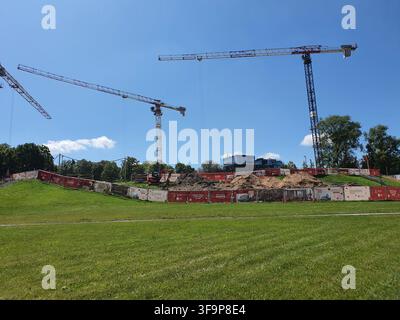 Baustelle mit mehreren Turmkranen vor einem klaren blauen Himmel. Zwei große Turmkrane dominieren die Szene, wobei ein dritter Kranausleger sichtbar ist auf Stockfoto