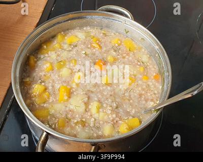 Ein Edelstahl-Topf gefüllt mit einer herzhaften Gemüsesuppe oder einem Eintopf steht auf einem schwarzen keramischen Elektroherd. Das Gericht enthält sichtbare Stücke von Stockfoto