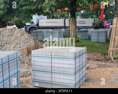 Baubaustellenszene, die mehrere Paletten mit grauen Betonpflastersteinen oder -blöcken zeigt, die mit grünen Kunststoffumreifungsbändern umwickelt sind. Im Stockfoto