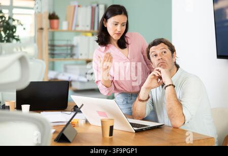 Wütende Chefin schreit einen männlichen Angestellten im Empfangsbereich an Stockfoto