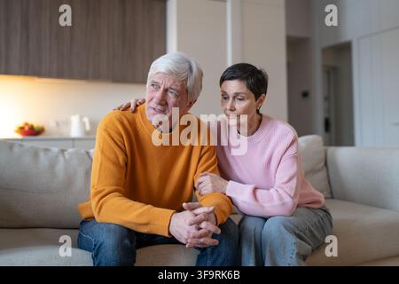 Mitfühlende Ehefrau, die stummen Beistand zu einem verstörten, aufgewühlten Ehemann leistet, der zusammen mit ihr auf der Couch sitzt. Stockfoto