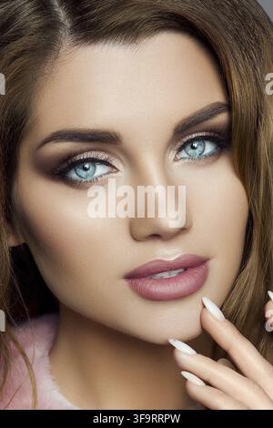 Studio Portrait von attraktiven gewellte blonde junge Frau mit blauen Augen und helle Professional Make-up Hand mit Maniküre tragen rosa samt Co Stockfoto