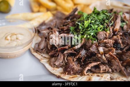 Arabisches traditionelles Fast Food. Geöffnetes gegrilltes Rindfleisch-Shawarma-Wrap auf einem Teller, serviert mit Pommes frites und Hummus. Rindfleisch-Doner Nahaufnahme. Niemand Stockfoto