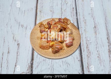 Knusprige Schweinebauch-Häppchen serviert auf rustikalem Pappteller über weiß getünchtem Holztisch Stockfoto