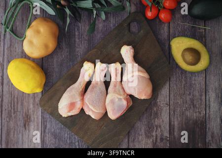 Rohe Hähnchen-Schenkel mit Gemüse auf einem Brett Stockfoto