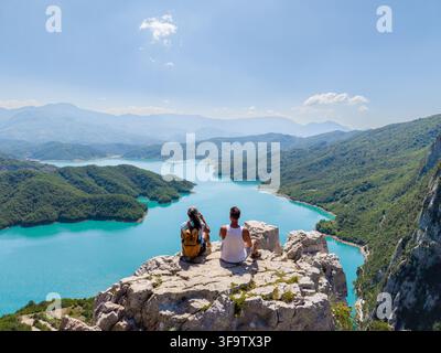 Zweierlei entspannt sich auf einem felsigen Vorsprung und bewundert das atemberaubende türkisfarbene Wasser des Bovilla-Reservoirs in Albanien. Dieser malerische Ort zeigt üppige grüne Landschaften und einen kristallklaren See unter strahlendem Himmel. Stockfoto