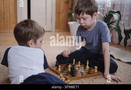 Kinder spielen Schach zu Hause, auf dem Boden sitzend Stockfoto