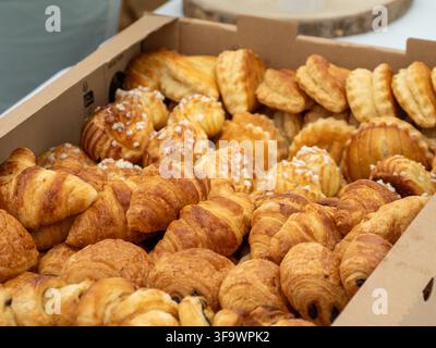Verschiedene frisch gebackene Croissants und Gebäck in einer Pappschachtel, bereit zum Servieren oder zum Verkauf. Stockfoto