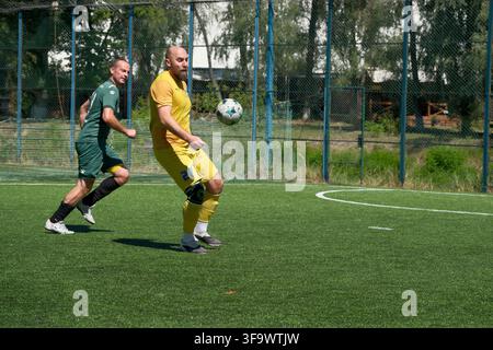 KIEW, UKRAINE - 16. AUGUST 2026: Amateur-Mini-Fußballspieler in gelber Uniform kontrolliert einen Fußball in der Luft mit seinem Körper, während ein Verteidiger Stockfoto