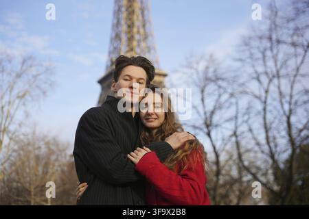 Ein glückliches Paar teilt eine herzliche Umarmung in der Nähe des Eiffelturms in Paris. Sie lächeln sich liebevoll an und genießen einen romantischen Moment zusammen Stockfoto