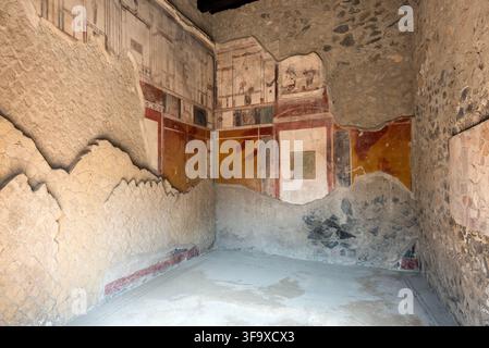 Verwitterte freskoverzierte Kammer mit rot, ocker und weiß bemalten Wandpaneelen im Haus der toskanischen Kolonnade im Archäologischen Park von Herculaneu Stockfoto