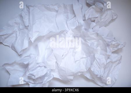 Zerknitterte weiße Papierstücke sind über eine ebene Fläche verteilt und zeigen einzigartige Texturen und Falten, die für künstlerische oder Designanwendungen geeignet sind Stockfoto