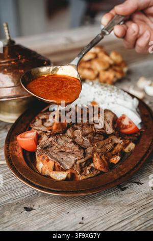Sämige Tomatensoße auf Iskender-Kapsalon gießen Stockfoto