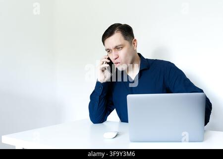 Ein junger Berufstätiger in einem dunkelblauen Hemd, der überrascht, gestresst oder tief konzentriert aussieht, während er telefoniert Stockfoto