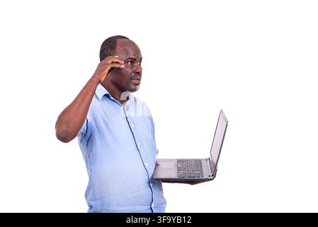 reifer Mann im Hemd steht vor weißem Hintergrund und telefoniert, während er einen Laptop hält. Stockfoto