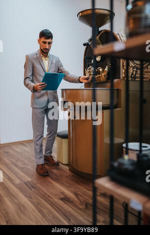 Geschäftsmann inspiziert eine gewerbliche Kaffeeröstmaschine im Röster, während er ein Klemmbrett hält und den Röstvorgang überwacht Stockfoto