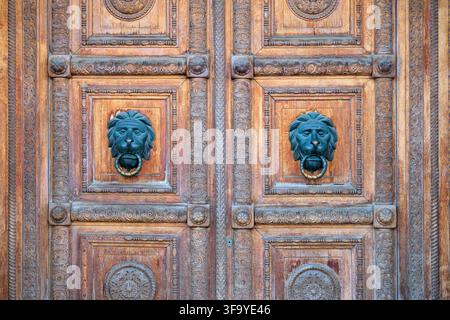 Verzierte hölzerne Doppeltür mit passenden Löwenkopf-Klöffeln und aufwendiger geschnitzter Dekoration. Historische Architektur, Erbeingang, Handwerkskunst, s Stockfoto
