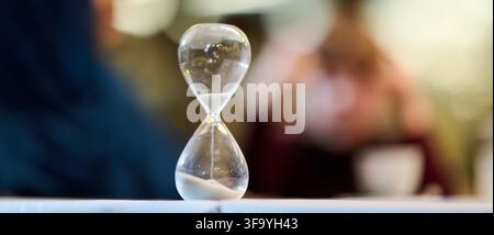 Sanduhr auf Tisch symbolisiert vergehende Zeit Geduld und Deadline in verschwommenem Interieurbild Stockfoto