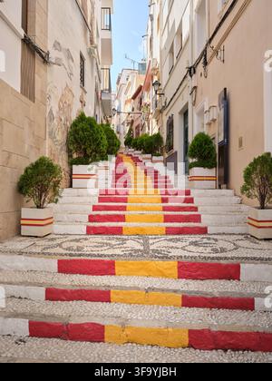 Bunte rot und gelb bemalte Treppen auf einer engen Altstadtstraße in Calpe, Spanien, eine unverwechselbare mediterrane ReiseSzene. Stockfoto