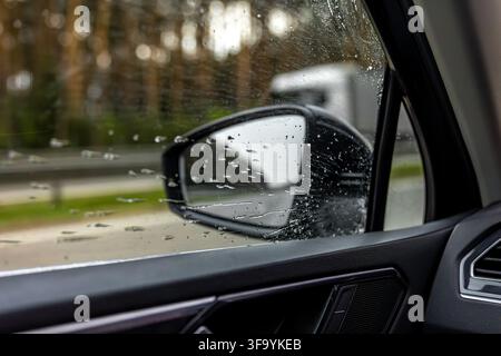 Regentropfen auf der Autoscheibe. Fahrzeuginfo mit Seitenspiegel und nasser Scheibe. Stockfoto