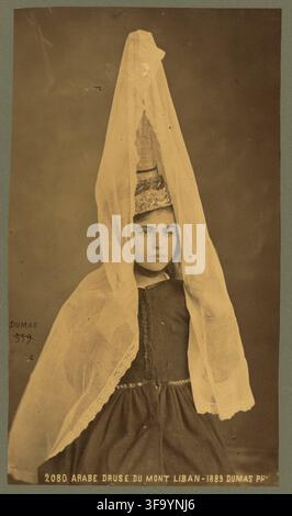 Albumen-Studio-Porträt einer namentlich nicht genannten jungen Druzenfrau aus dem Libanongebirge, fotografiert im Jahr 1889 vom italienischen Fotografen aus Beirut Tancrède R. Dumas. Sie trägt einen hohen kegelförmigen Kopfschmuck unter einem durchsichtigen Schleier und ein traditionelles Kleid. Die historische französische Bildunterschrift lautet „Arabe druse du Mont Liban“; die damalige Terminologie wird als Inschrift beibehalten, während die moderne Identifizierung eine Druzenfrau beschreibt. Der Libanon war damals in der Osmanischen Syrien, heute Libanon. Stockfoto
