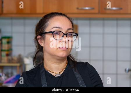 Eine Frau mit Brille blickt zur Seite, während sie in einer Küche steht. Stockfoto