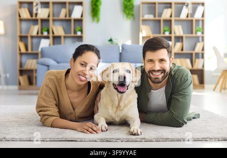 Fröhliches Paar liegt mit Labrador zu Hause, Haustierporträt in hellem Wohnzimmer Stockfoto