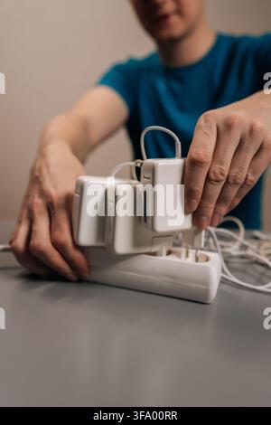Vertikal beschnittene Aufnahme einer Person, die das Laptop-Ladegerät in eine weiße Steckdosenleiste einsteckt und tragbare Elektronik an eine Steckdose anschließt, um sie aufzuladen Stockfoto